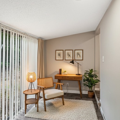 Room with a sliding door window small desk with a chair, lamp and decor on the walls