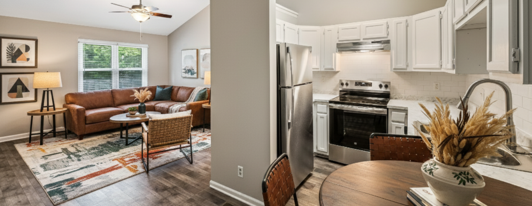 Open-concept living room, dining area, and kitchen at Jamestown Landing Apartments featuring vaulted ceilings, a skylight, stainless steel appliances, and wood-style flooring.