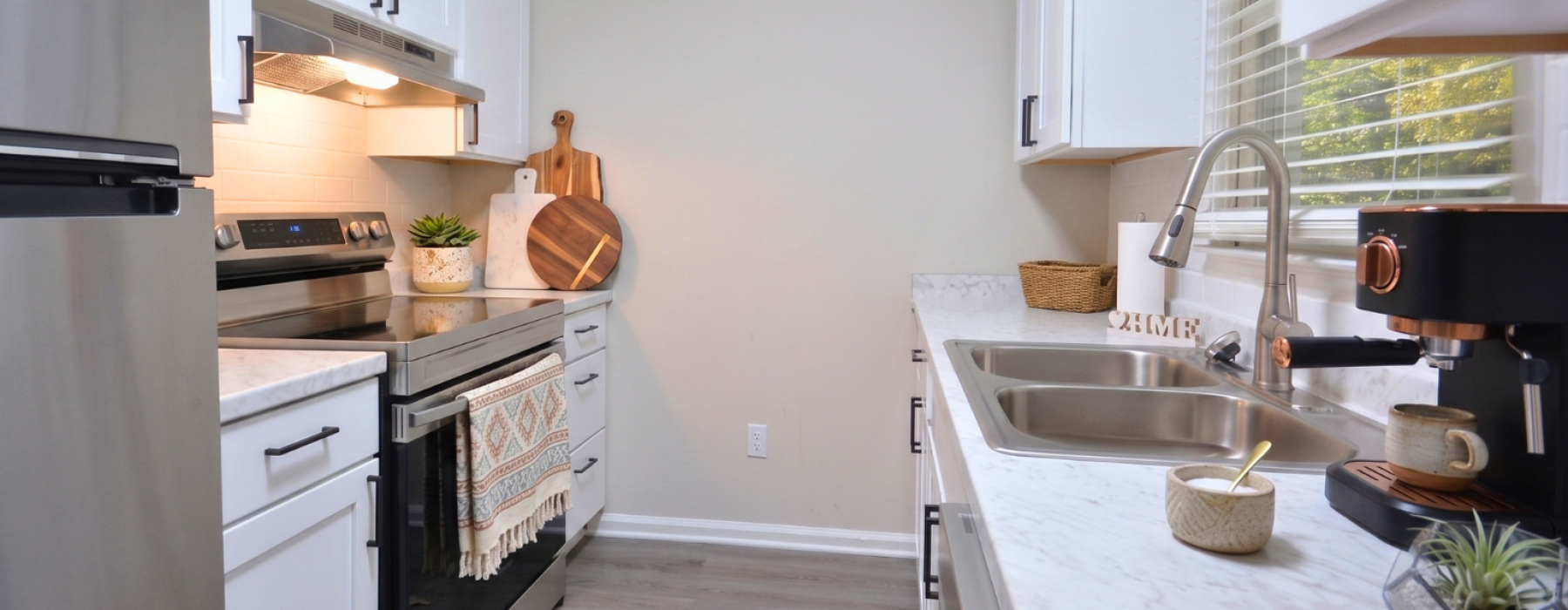 Renovated kitchen at Sherrill Place Apartments featuring stainless steel appliances, white shaker-style cabinetry, black hardware, subway tile backsplash, and marble-inspired countertops.